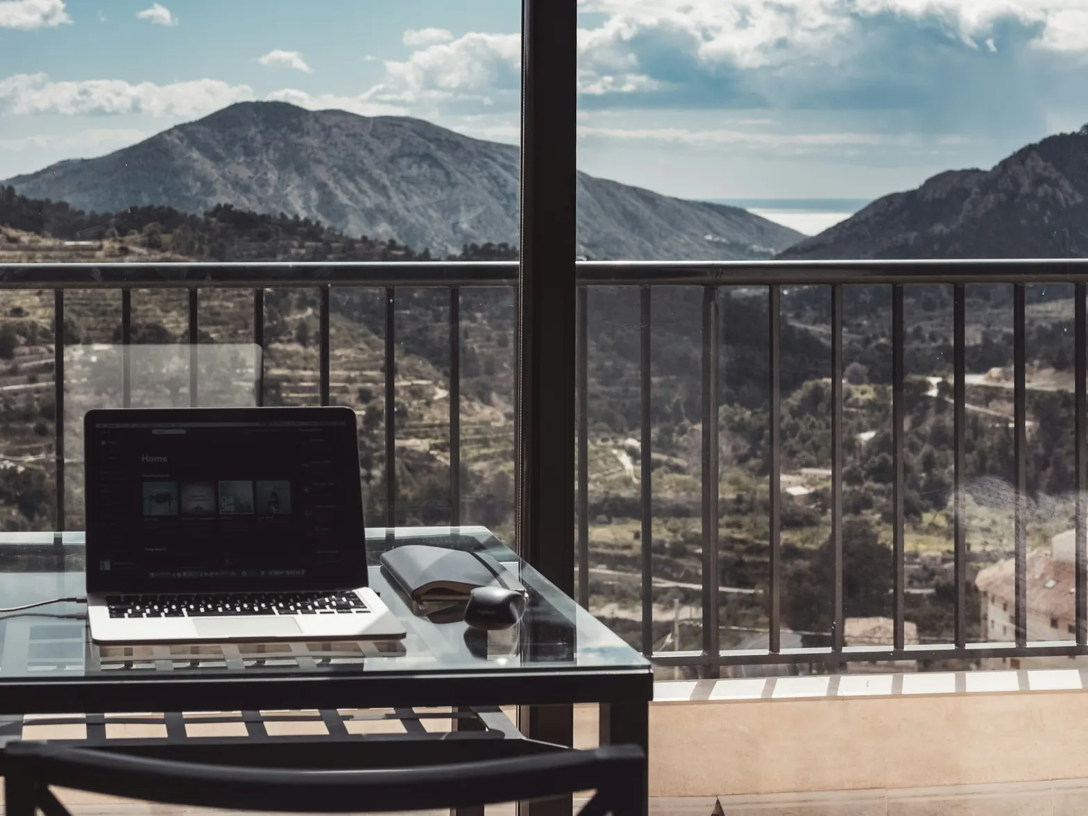 A laptop on a table on a balcony, looking out over terraced hills