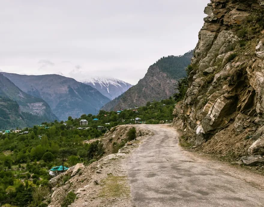 A dirt road cut into a cliff above a green valley in Himachal Pradesh